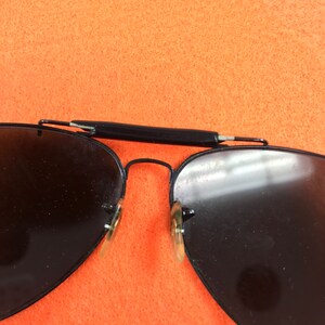 Puede incluir: Gafas de sol aviador negras con lentes oscuros y montura de metal negro.