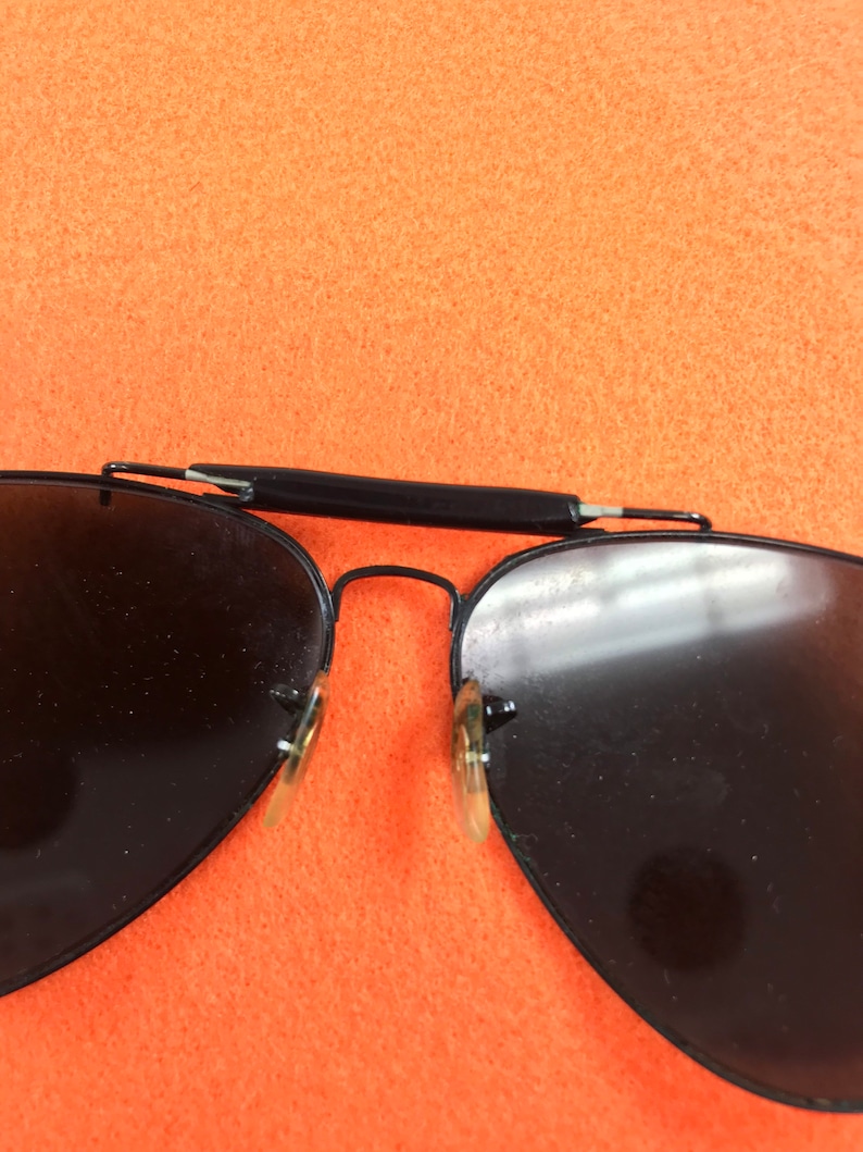 Puede incluir: Gafas de sol aviador negras con lentes oscuros y montura de metal negro.