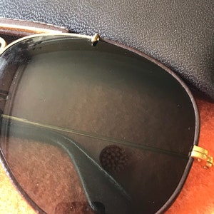 Op de afbeelding: Een paar klassieke aviator-zonnebrillen met bruine glazen en een gouden metalen frame. De zonnebril ligt op een bruin oppervlak.