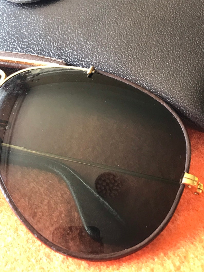 Op de afbeelding: Een paar klassieke aviator-zonnebrillen met bruine glazen en een gouden metalen frame. De zonnebril ligt op een bruin oppervlak.