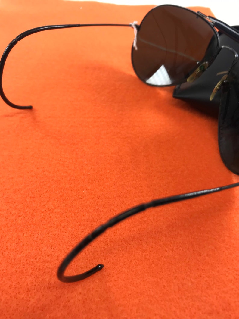 Puede incluir: Gafas de sol aviador negras con montura de metal y lentes oscuras. Las gafas est&aacute;n plegadas y las patillas est&aacute;n dobladas en forma de gancho.