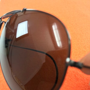 Puede incluir: Primer plano de unas gafas de sol aviador marrones con montura negra. Las gafas de sol reflejan una fuente de luz brillante.