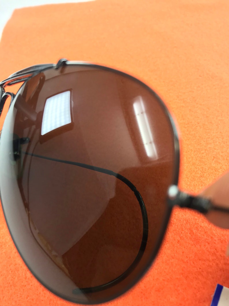 Puede incluir: Primer plano de unas gafas de sol aviador marrones con montura negra. Las gafas de sol reflejan una fuente de luz brillante.