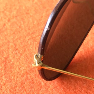 Op de afbeelding: Close-up van het gouden scharnier van een zonnebril. Het scharnier is gemaakt van metaal en heeft een veermechanisme.