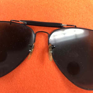 Puede incluir: Gafas de sol aviador negras con montura de metal y lentes oscuras. Las gafas est&aacute;n dobladas por la mitad.