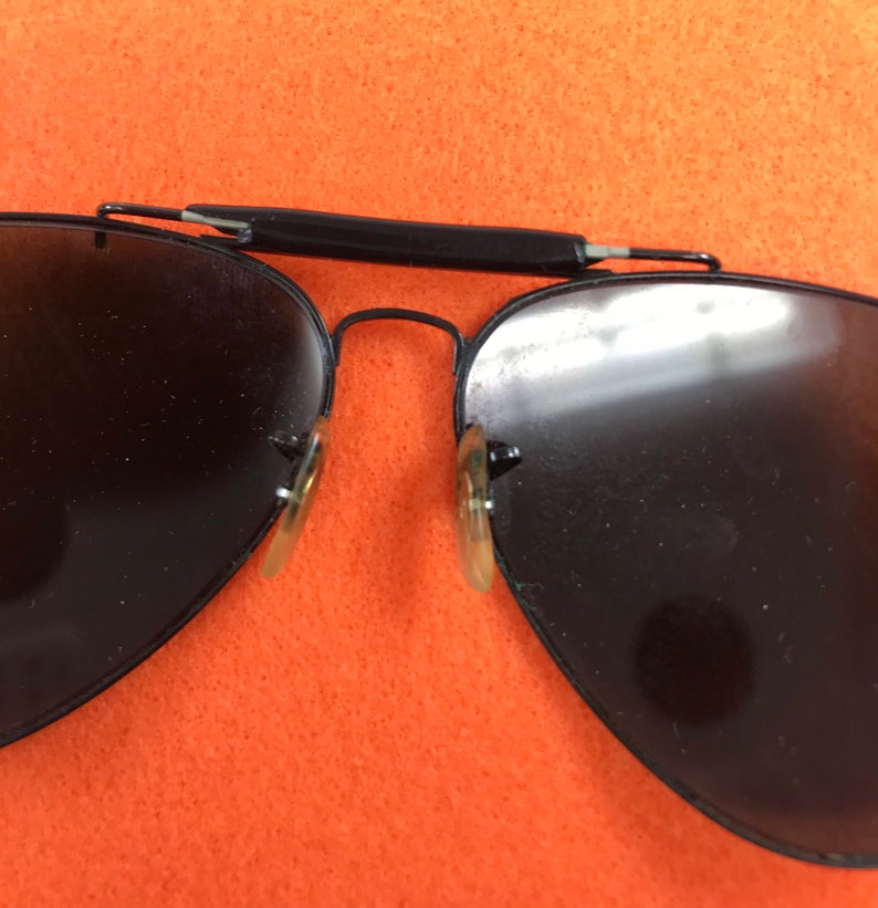 Puede incluir: Gafas de sol aviador negras con montura de metal y lentes oscuras. Las gafas est&aacute;n dobladas por la mitad.