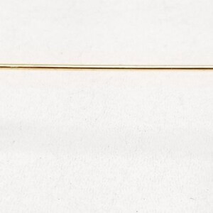 May include: A close-up of the gold metal arm of a pair of glasses. The arm has a brown plastic tip.