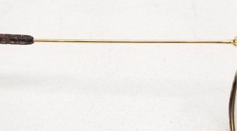May include: A close-up of the gold metal arm of a pair of glasses. The arm has a brown plastic tip.