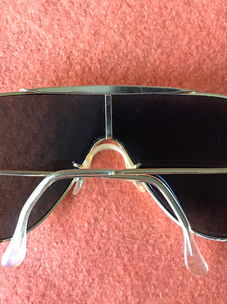 May include: Gold-tone aviator sunglasses with a double bridge and dark lenses. The sunglasses have a classic design and are in good condition.