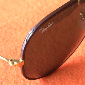 Op de afbeelding: Close-up van een bruine Ray-Ban aviator zonnebril met gouden accenten. De zonnebril heeft een bruin lederen montuur en donkere glazen.