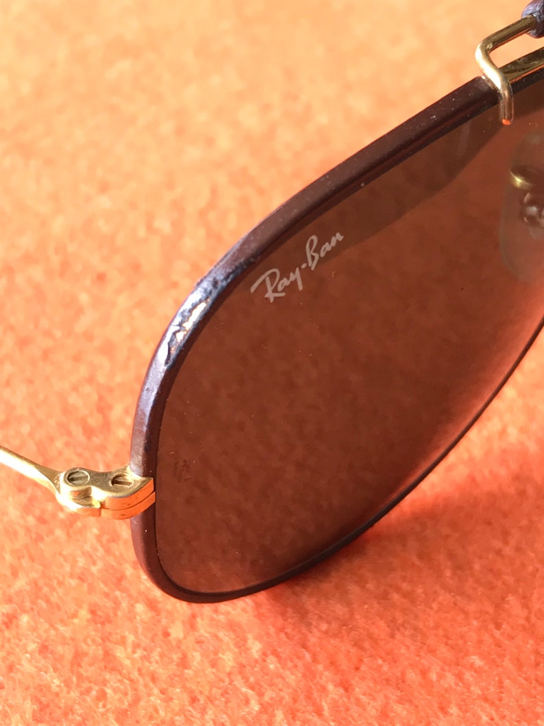 Op de afbeelding: Close-up van een bruine Ray-Ban aviator zonnebril met gouden accenten. De zonnebril heeft een bruin lederen montuur en donkere glazen.