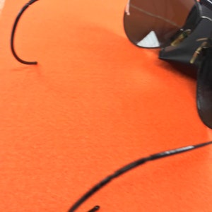 Puede incluir: Gafas de sol aviador negras con lentes oscuros y una funda de cuero negra. Las gafas tienen un fino marco de metal y est&aacute;n dobladas por la mitad.