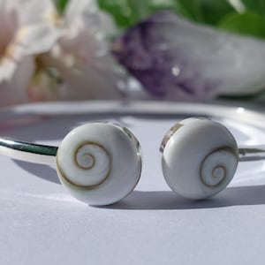 May include: A silver bangle bracelet with two white shell charms. The shells have a brown spiral pattern.