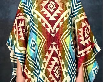 May include: A colorful poncho with a geometric pattern in shades of red, blue, green, and cream. The poncho has a hood and fringed edges. The design features diamond and triangle shapes. The garment is worn by a person.