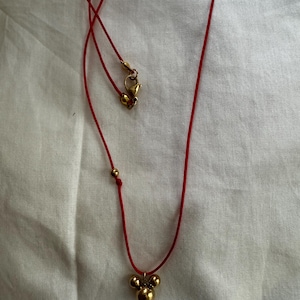 May include: A red string necklace with a gold charm featuring three connected spheres.