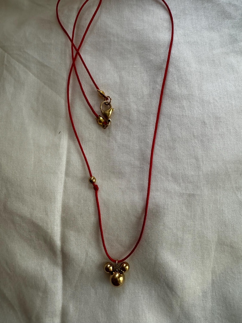 Peut inclure: Un collier en cordon rouge avec un pendentif en or compos&eacute; de trois sph&egrave;res reli&eacute;es.