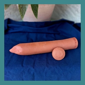Può includere: Un oggetto cilindrico color terracotta con un'estremità appuntita e un piccolo disco rotondo. Gli oggetti poggiano su un tessuto blu. Il testo "Les Demains dans la Terre" è nella parte superiore dell'immagine.