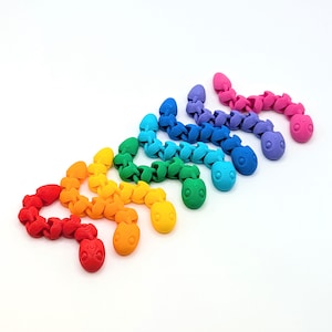 May include: A collection of colorful, articulated snake toys in a rainbow of hues. Each snake features a segmented body and a detailed head, with colors ranging from red to pink. The toys are arranged on a white surface.
