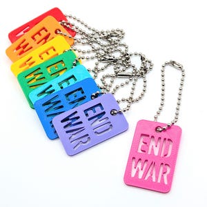 May include: A collection of colorful dog tag pendants with the words "END WAR" cut out. The tags are in a rainbow of colors, including red, orange, yellow, green, blue, and purple, each attached to a silver ball chain.