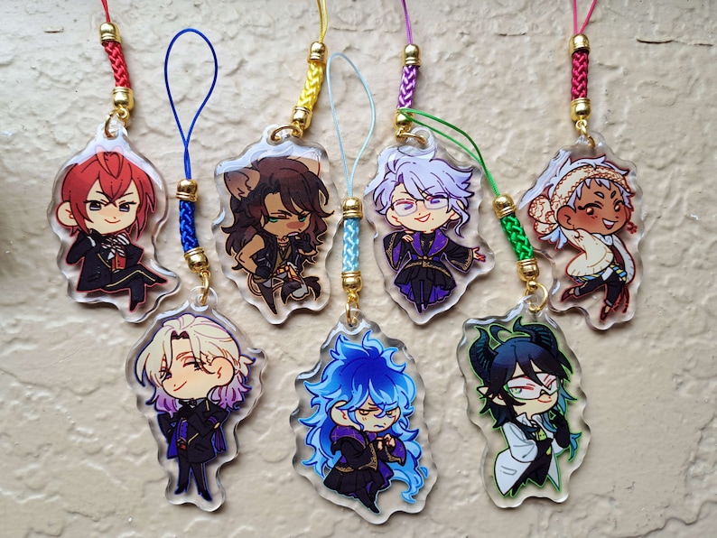 Puede incluir: Conjunto de ocho amuletos de personajes de anime coloridos con fondos de acr&iacute;lico transparente y anillos de metal dorados. Cada amuleto presenta un personaje diferente con detalles y expresiones &uacute;nicos. Los amuletos est&aacute;n unidos a cordones de cuerda coloridos con cuentas doradas.