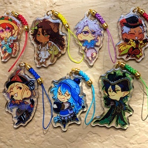 Op de afbeelding: Set van zeven kleurrijke anime-personagecharms met verschillende ontwerpen. Elke charm heeft een ander personage met unieke kleding en accessoires. De charms zijn bevestigd aan kleurrijke touwtjes.