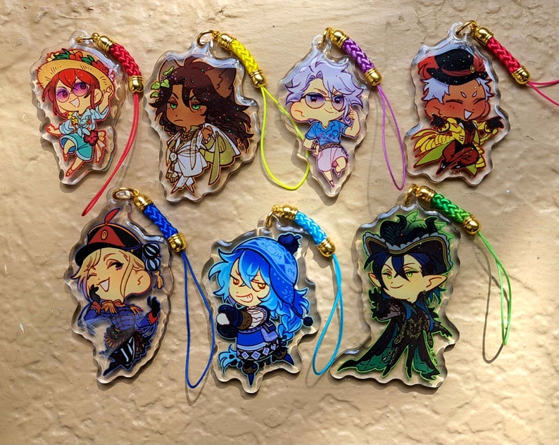 Op de afbeelding: Set van zeven kleurrijke anime-personagecharms met verschillende ontwerpen. Elke charm heeft een ander personage met unieke kleding en accessoires. De charms zijn bevestigd aan kleurrijke touwtjes.