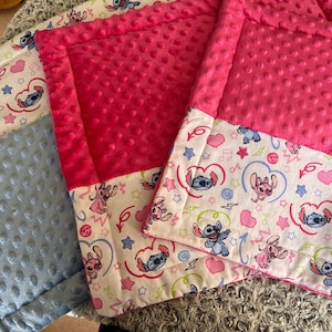Peut inclure: Trois couvertures pour bébé sur le thème du personnage Stitch. Une couverture est bleu clair et deux sont rose vif. Les couvertures ont une bordure à motifs avec Stitch, des cœurs, des étoiles et des notes de musique. Les couvertures sont en tissu doux et texturé.