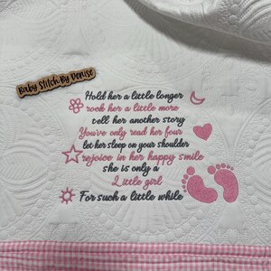 May include: A white quilted blanket with a pink gingham border featuring embroidered text that reads: Hold her a little longer, rock her a little more, tell her another story, You've only read her four, let her sleep on your shoulder, rejoice in her happy smile, she is only a little girl, For such a little while. Includes pink icons of a flower, moon, heart, star, sun, and baby footprints.