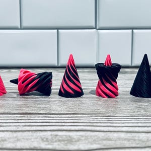 May include: A collection of five decorative, cone-shaped objects. The objects feature a spiral design with alternating black and bright pink stripes. One object is solid pink, and another is solid black.