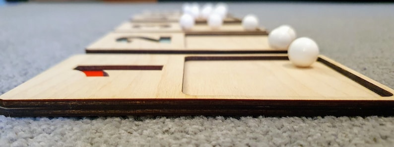 May include: Wooden tray with the number 1 and a slot for a white marble. The tray is part of a set of trays with numbers 1 through 5.