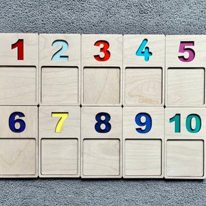 May include: A set of ten wooden tiles with numbers 1 through 10. Each tile has a different coloured number, including red, blue, yellow, green, and light blue.