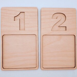 May include: Two wooden number trays with a raised number on the top and a recessed area on the bottom. The first tray has the number "1" and the second tray has the number "2".