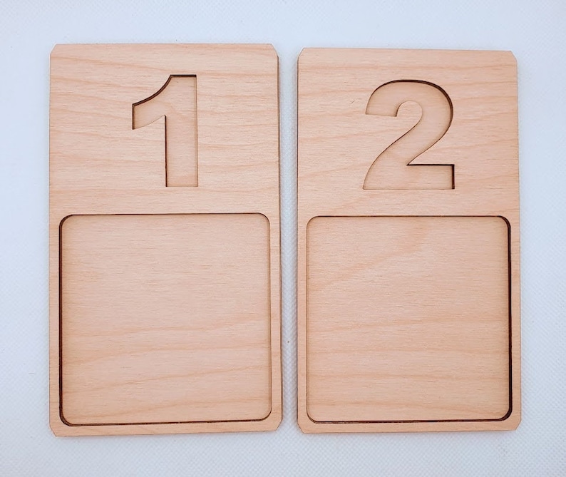 May include: Two wooden number trays with a raised number on the top and a recessed area on the bottom. The first tray has the number "1" and the second tray has the number "2".