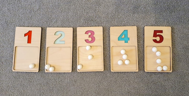 May include: Five wooden blocks with numbers 1 to 5 printed in red and blue. Each block has a corresponding number of white balls inside.