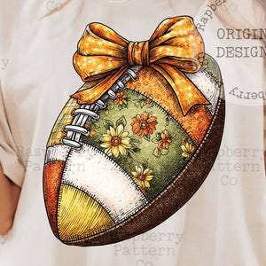 May include: A decorative football with a large orange bow. The football features a patchwork design with floral patterns and a mix of colors including green, orange, and brown. The image has the text "ORIGINAL DESIGNER".
