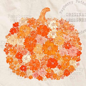 May include: A cream-coloured t-shirt with a floral pumpkin design in shades of orange, peach, and pink. The shirt is made of a soft material and has the text "ORIGINAL DESIGNER" printed on it. A fall-themed graphic tee.