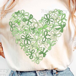May include: A white t-shirt with a green heart design made of bows. The text "Raspberry Pattern Co. sublimation design" is printed below the heart.
