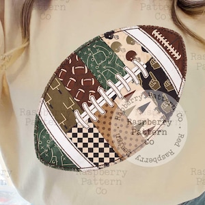 May include: A cream-colored crewneck sweatshirt featuring a large, central graphic of an American football. The football design is composed of various patterned sections including green play diagrams, brown and white checkers, and polka dots.