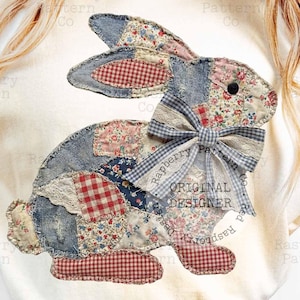 Könnte beinhalten: Cremefarbenes T-Shirt mit einem Patchwork-Hasen-Design. Der Hase besteht aus verschiedenen Stoffen in Rot-, Blau- und Blumenmustern, mit einer blau-weiß karierten Schleife. Der Text "ORIGINAL DESIGNER" ist sichtbar.