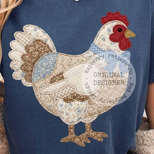 Könnte beinhalten: Ein marineblaues T-Shirt mit einem Patchwork-Hühner-Design. Das Huhn hat einen roten Kamm, eine blaue Fliege und besteht aus verschiedenen gemusterten Stoffen in Braun-, Blau- und Weißtönen. Der Text "Raspberry Pattern Co" und "Original Designer" ist aufgedruckt.