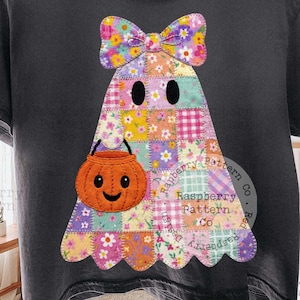 May include: A charcoal grey short-sleeve t-shirt featuring a central graphic of a ghost made of a colourful floral and plaid patchwork pattern. The ghost has a large matching bow on its head and is holding a small orange jack-o'-lantern bucket.