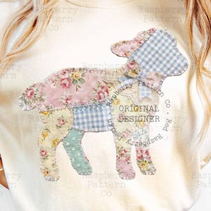 May include: A cream-coloured t-shirt with a patchwork lamb design. The lamb is made from floral and gingham fabrics in pastel shades. The text "ORIGINAL DESIGNER" is printed on the shirt. The shirt is worn with blue jeans.