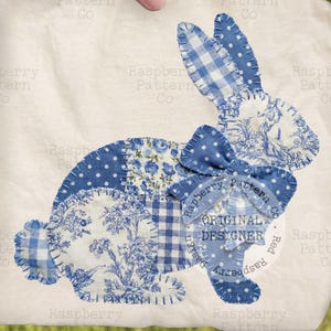 May include: A white square fabric with a patchwork bunny design. The bunny is made of blue patterned fabrics, including floral, polka dot, and gingham patterns. A blue bow is at the neck. The text "ORIGINAL DESIGNER" is visible.