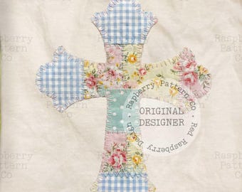 May include: A cream-colored, quilted cross with a patchwork design. The cross features sections of blue gingham, floral patterns, and a dotted teal fabric. The text "ORIGINAL DESIGNER" is in a circle.