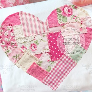 Puede incluir: Un artículo de tela blanca con un gran corazón de patchwork en varios tonos de rosa. El diseño del corazón incorpora patrones florales, de lunares y a rayas. Se puede leer el texto "Raspberry Pattern Co. ORIGINAL DESIGNER".