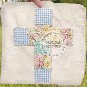 May include: A cream-colored, square fabric item with a cross design. The cross is made of patchwork squares in blue gingham, floral patterns, and lace. The center of the cross has a circular design with the text "ORIGINAL DESIGNER".