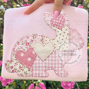 Peut inclure: Un tissu rectangulaire rose clair avec un motif de lapin en patchwork. Le lapin présente des accents en forme de cœur et divers motifs roses et blancs. Le texte "ORIGINAL DESIGNER" est visible.