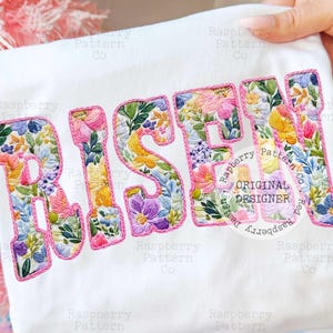 Könnte beinhalten: Weißes Textil mit dem Wort "RISEN", das mit bunten Blumenmustern bestickt ist. Die Buchstaben sind mit rosa Faden umrandet. Das Design enthält den Text "Raspberry Pattern Co" und "Original Designer".