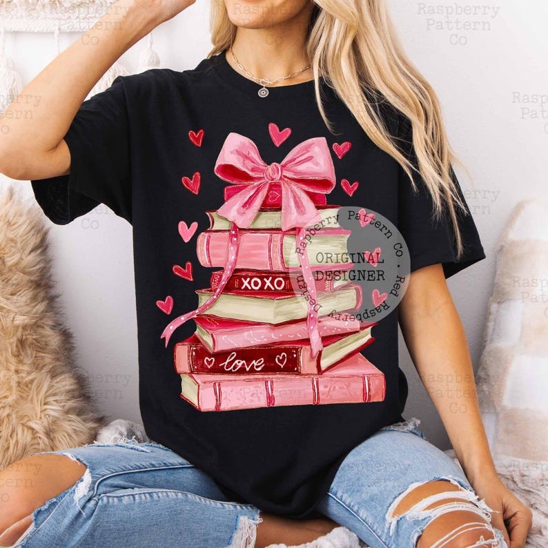 May include: Black t-shirt featuring a stack of pink books tied with a pink ribbon and bow. The books have the words "XOXO" and "love" on them, with pink hearts scattered around. The shirt has the text "Raspberry Pattern Co. Original Designer".
