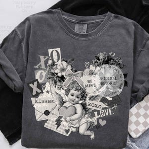 May include: Dark gray sweatshirt with a vintage-style graphic featuring a cherub holding a heart, surrounded by floral elements, the words "XOXO", "LOVE", and "kisses". The text "BE MINE" and "ORIGINAL DESIGNER" are also present.